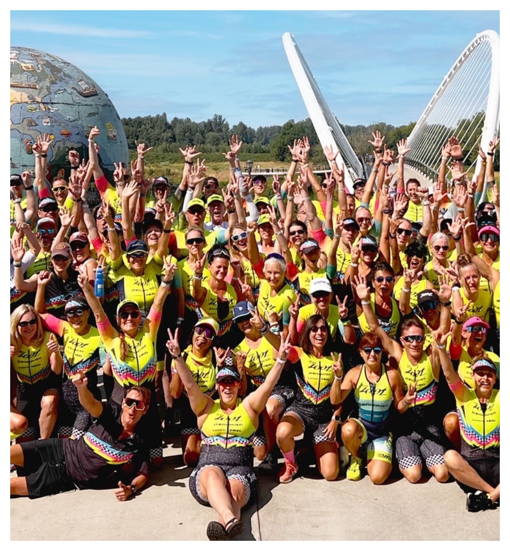 A large group of Team Zoot athletes smiling with hands up in neon yellow kits outside.